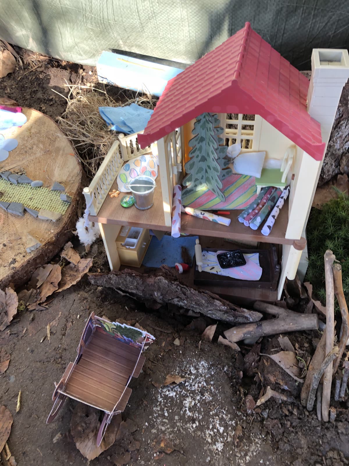 Puppenhaus im Matsch aufgebaut, daneben eine kleine Schubkarre